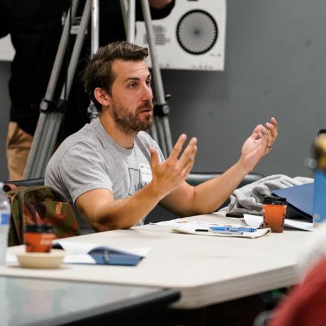 Man speaking to people behind a desk. 