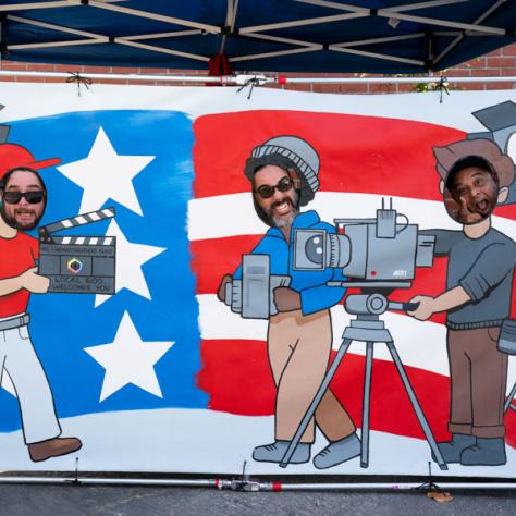 Photo of men behind painted cut out photo screen. 