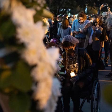 Crowd at a vigil with blurry flowers in the foreground. 