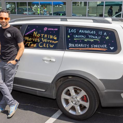 Writing on car window and man standing next to car. 