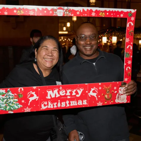 People posing for photo together in Merry Christmas frame. 