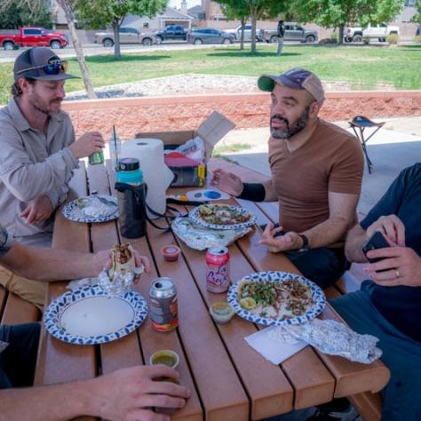 People talking and eating at a picnic table. 