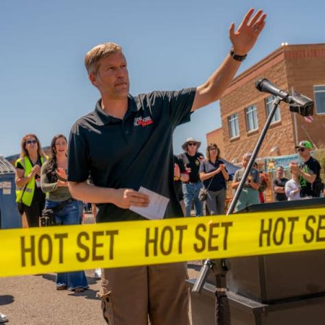 Man speaking into microphone with yellow tape in front of him.