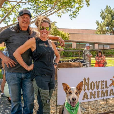 People posing for photo in front of Novel Animals sign. 