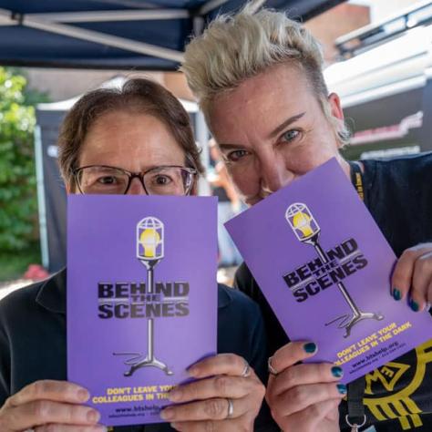 Two people posing with purple pamphlets. 