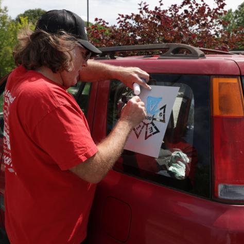 Person writing on car sign. 