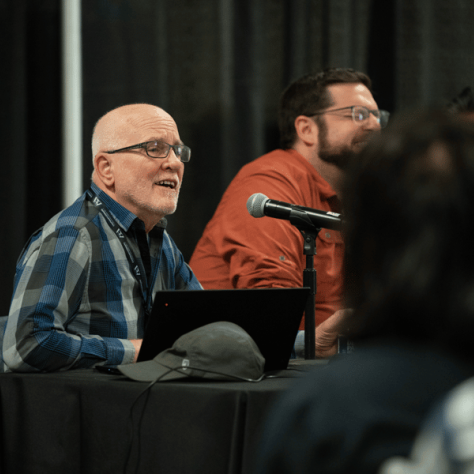 Man sitting at a table talking into a mic. 