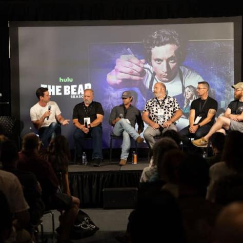 Panel of people sitting on stage behind screen. 