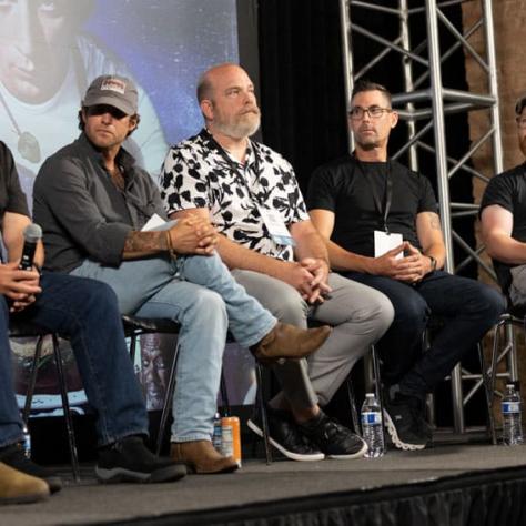 Panel of people sitting on stage behind screen. 