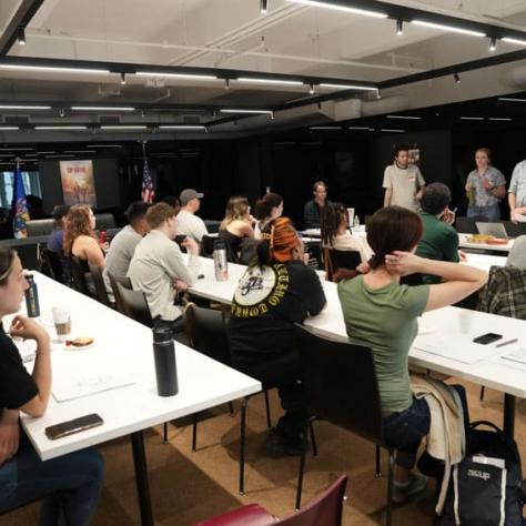 People sitting at tables watching people at the front of the room. 