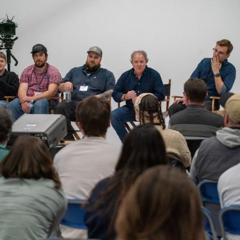 People sitting and speaking in front of an audience. 