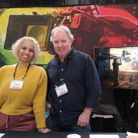 Two people posing for photo in front of table. 