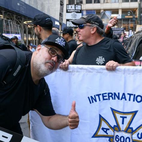 Man posing with thumbs up and banner. 