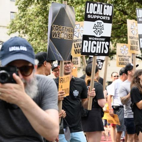 Man taking a photo, people in background marching with signs. 