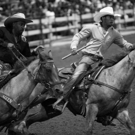 Black and white of two men on horses. 