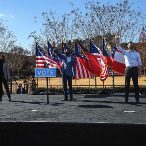 People standing on stage with fists up in front of flags. 