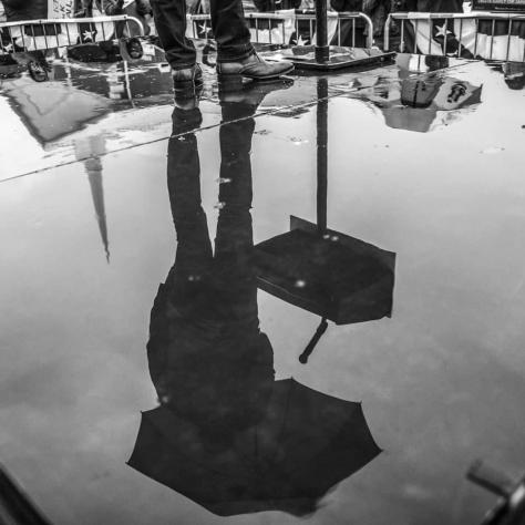 Black and white photo of man on stage with umbrellas reflection. 