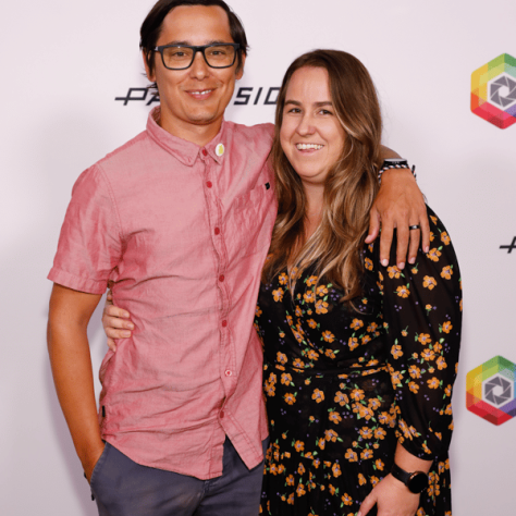 Two people posing in front of backdrop. 