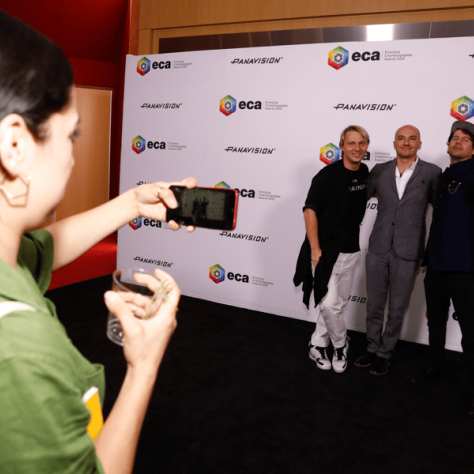 Woman in green taking photo of people in front of a backdrop. 