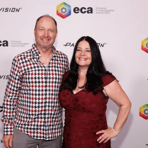 Two people posing for photo in front of backdrop. 