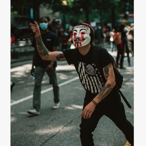 Person with a mask and black t shirt with hand in the air in the street. 