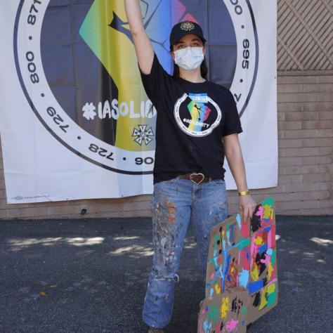 Person posing with fist in the air in front of backdrop. 