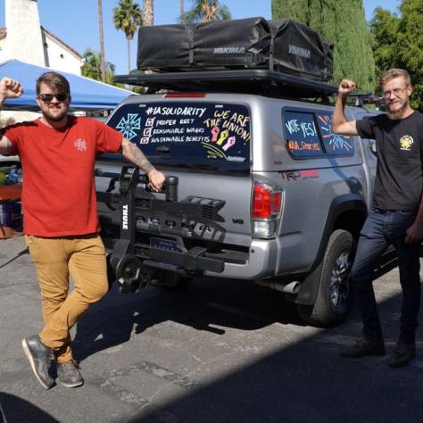 People posing with fists up next to a decorated car. 