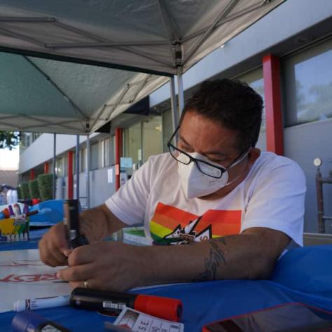 Person sitting at a table writing on a sign. 