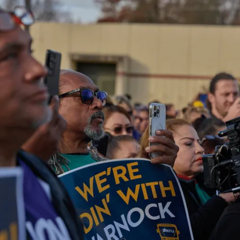 People watching, holding cameras and signs. 