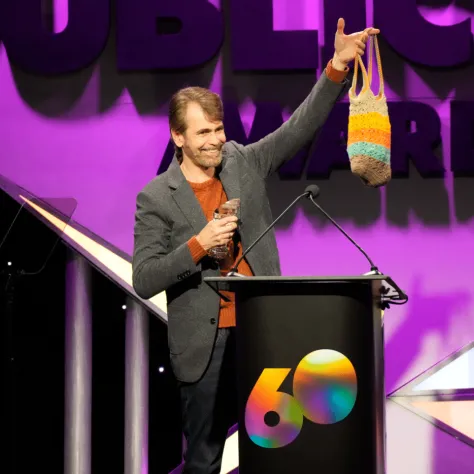 Man on stage at podium holding bag in the air. 