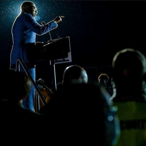 Dark photo of man speaking on stage. 