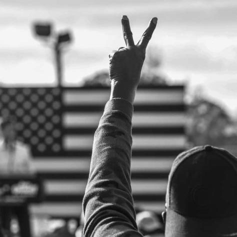 Black and white photo of someone with the peace sign in the air. 