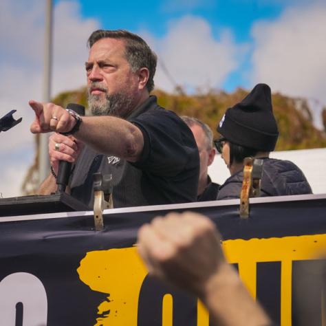 People speaking into microphones at rally. 