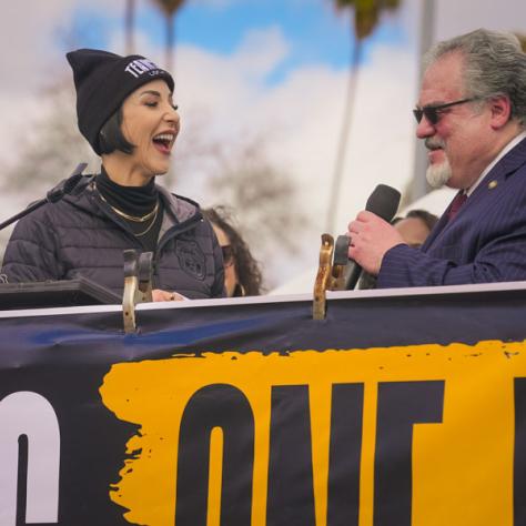 People speaking into microphones at rally. 