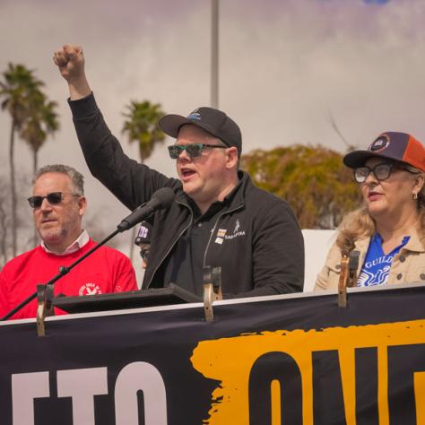 People speaking into microphones at rally. 