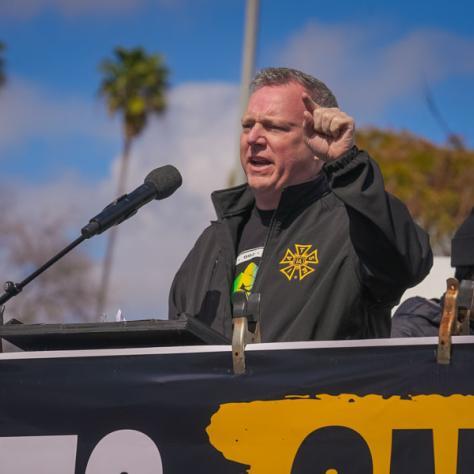 People speaking into microphones at rally. 