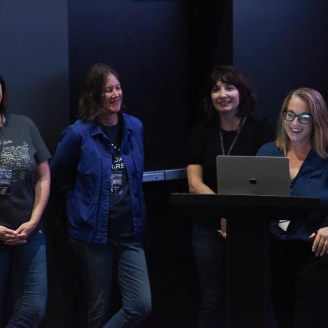 Photo of people standing together and looking at laptop. 