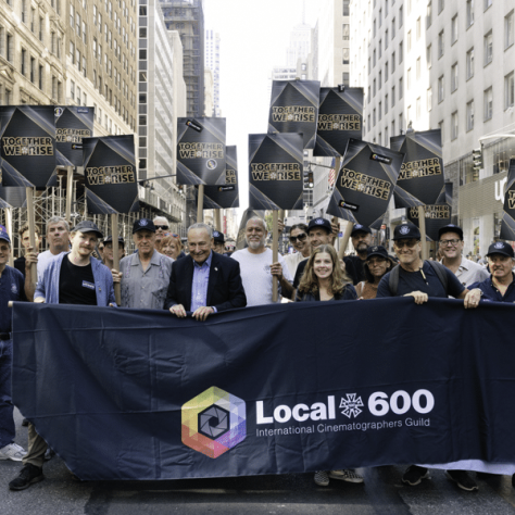 People marching in a parade with a banner and signs. 