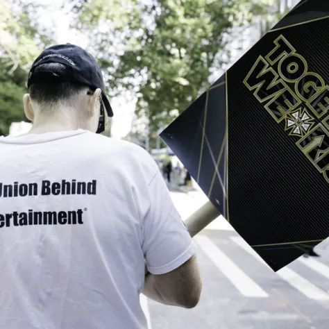 Back view of a man marching in a parade with a sign. 