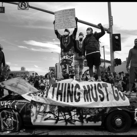 People standing on a wrecked cop car holding signs and fists in the air. 