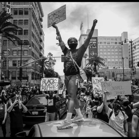 Crowd at a protest with person standing on a car with sign. 