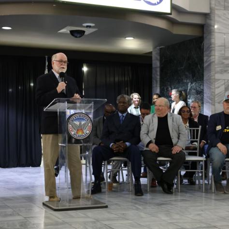 Man speaking in front of people at a podium. 