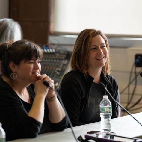 Two women sitting at table with mics. 