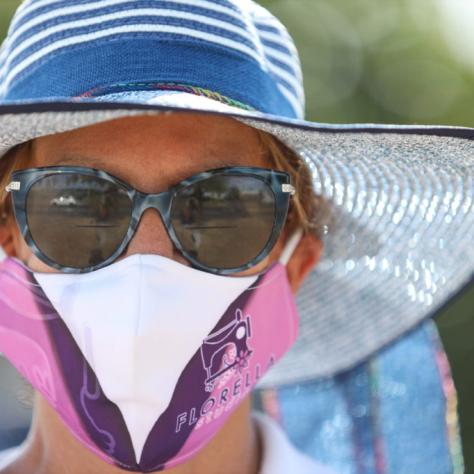 Close up of woman in brimmed hat and white, pink, and purple mask. 