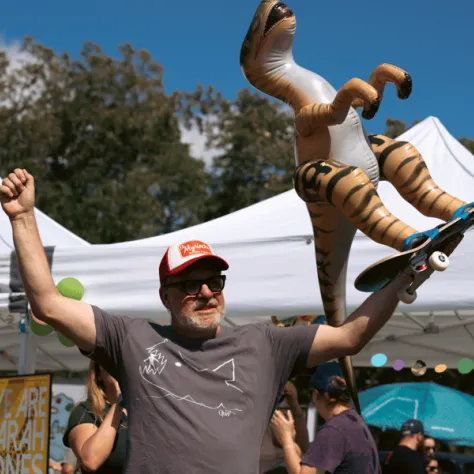 Man holding dinosaur on a skateboard in the air. 