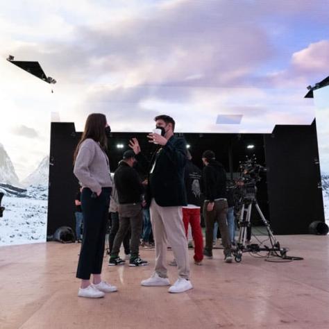 Two people talking in front of a mountain backdrop. 