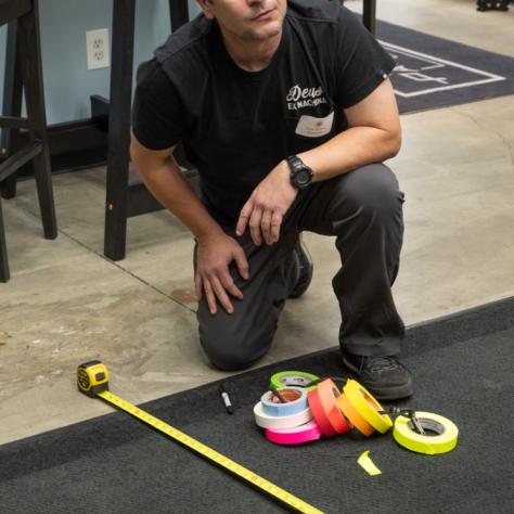 A man with a lot of colored tape measures the floor with a tape measure