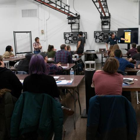 Man points to a screen in front of seated students