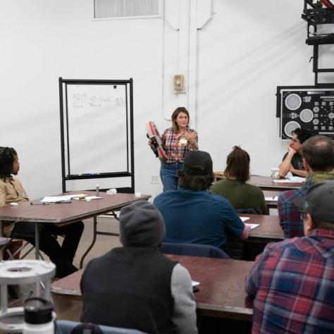 Woman holding a film loader speaks in front of seated students