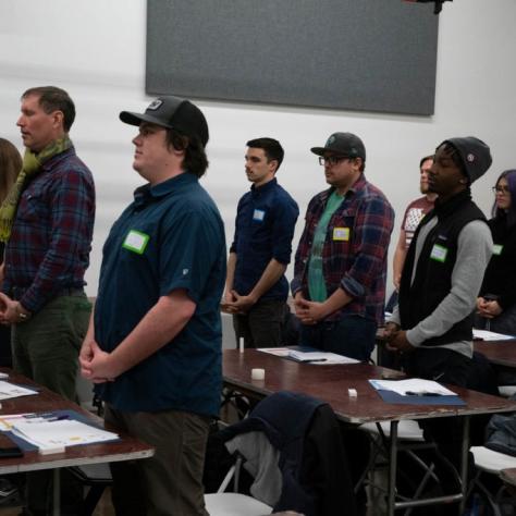 Students standing in front of tables with their hands clasped in front